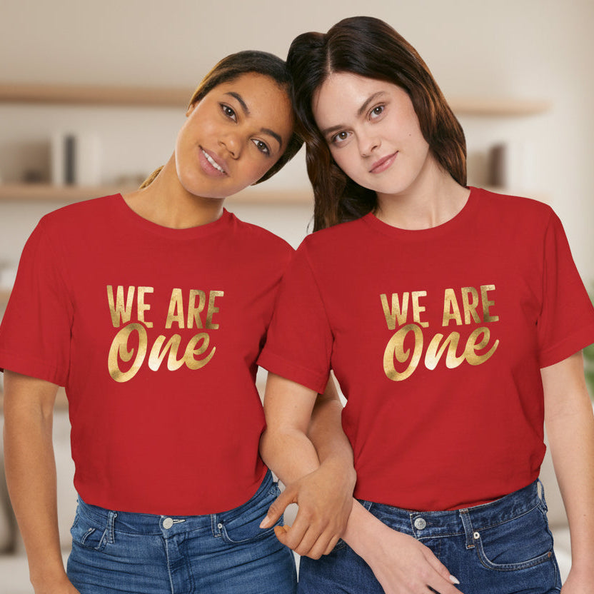 Two people wearing red t-shirts with the text 'WE ARE ONE' in gold